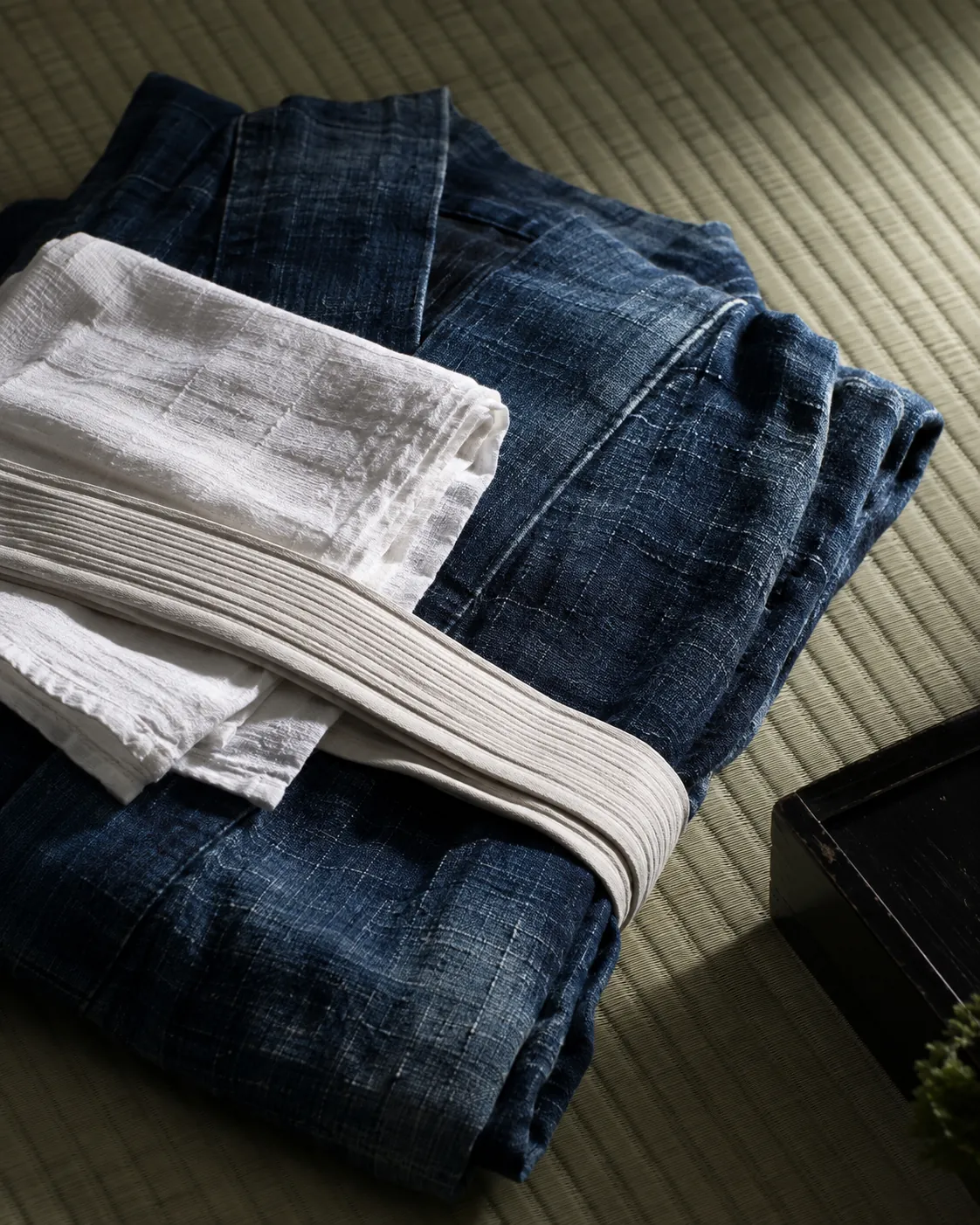 A folded indigo linen yukata with a white sash and towel on tatami