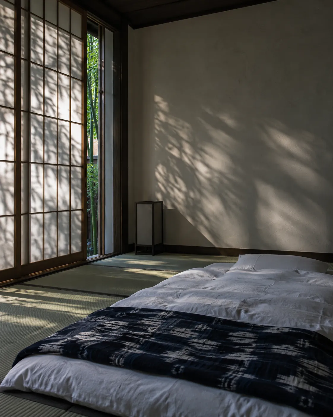 A futon with an indigo kasuri cover on tatami, bamboo shadows moving on the shoji
